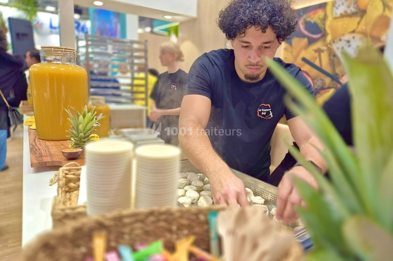 Un homme prépare des aliments dans un stand, avec des gobelets empilés et une grande jarre de jus en arrière-plan.