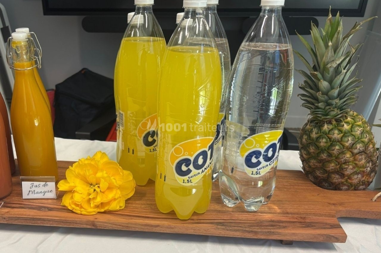Bouteilles de soda jaune et d'eau pétillante sur une planche en bois, avec une fleur jaune et un ananas à côté.