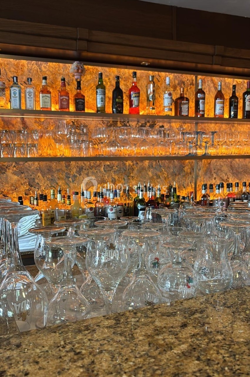 Rayonnages de bar avec bouteilles d'alcool variées et verres disposés sur un comptoir en pierre.
