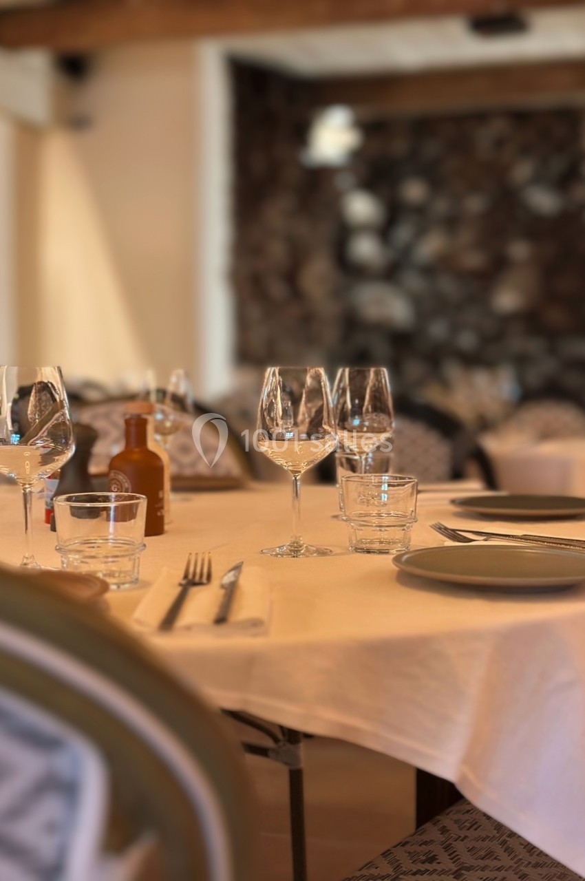 Table dressée avec nappes blanches, verres à vin, assiettes et couverts dans un restaurant à l'ambiance chaleureuse.