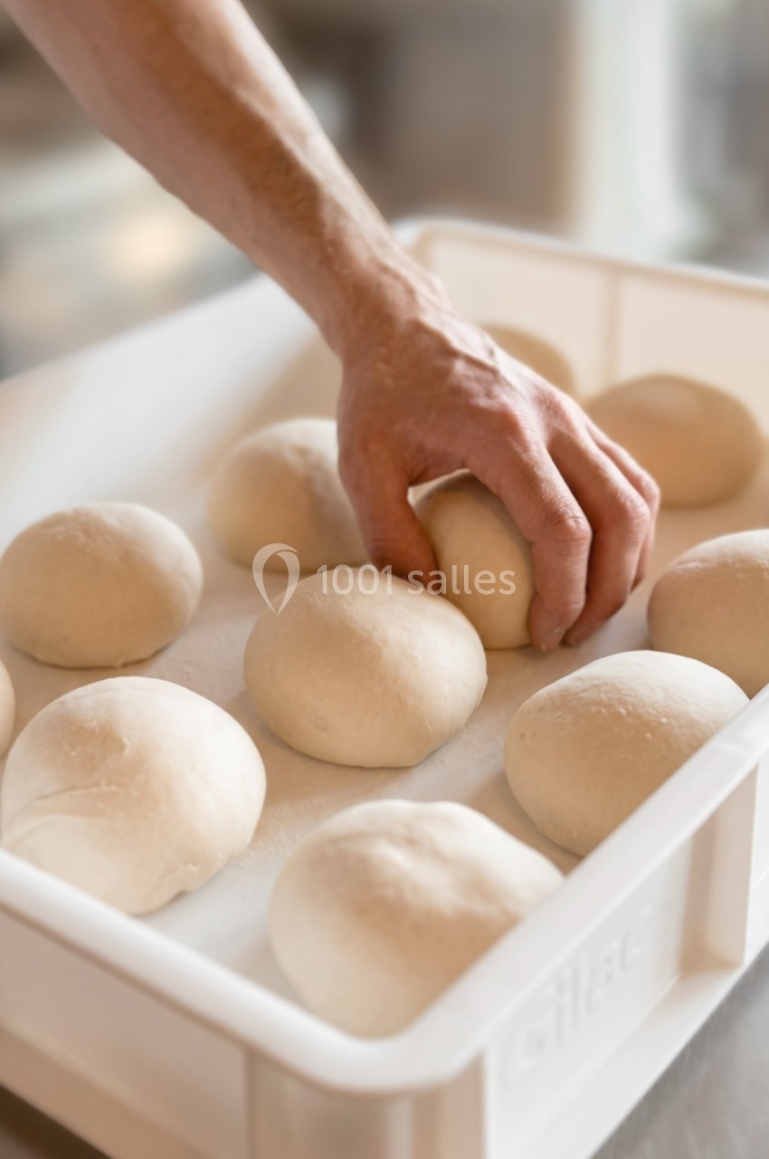 Main ajustant des boules de pâte levée dans un bac en plastique blanc sur une surface de travail.