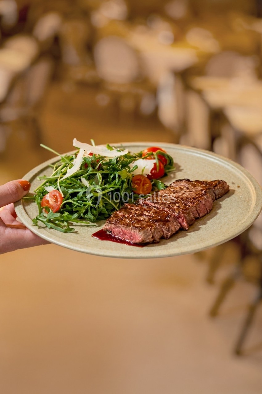 Assiette contenant un steak grillé et une salade de roquette avec tomates cerises, servie dans un restaurant.