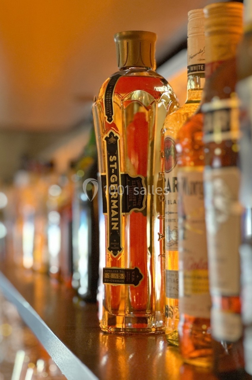 Bouteilles d'alcool alignées sur une étagère éclairée, avec une bouteille de liqueur St-Germain mise en avant.