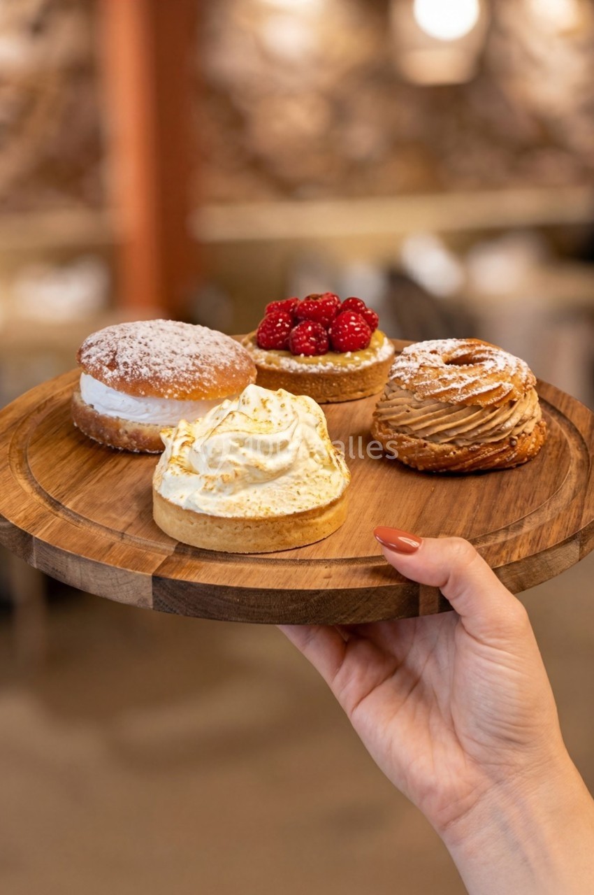 Plateau en bois tenu à la main, présentant quatre pâtisseries variées, dont une tarte aux framboises et un chou à la crème.