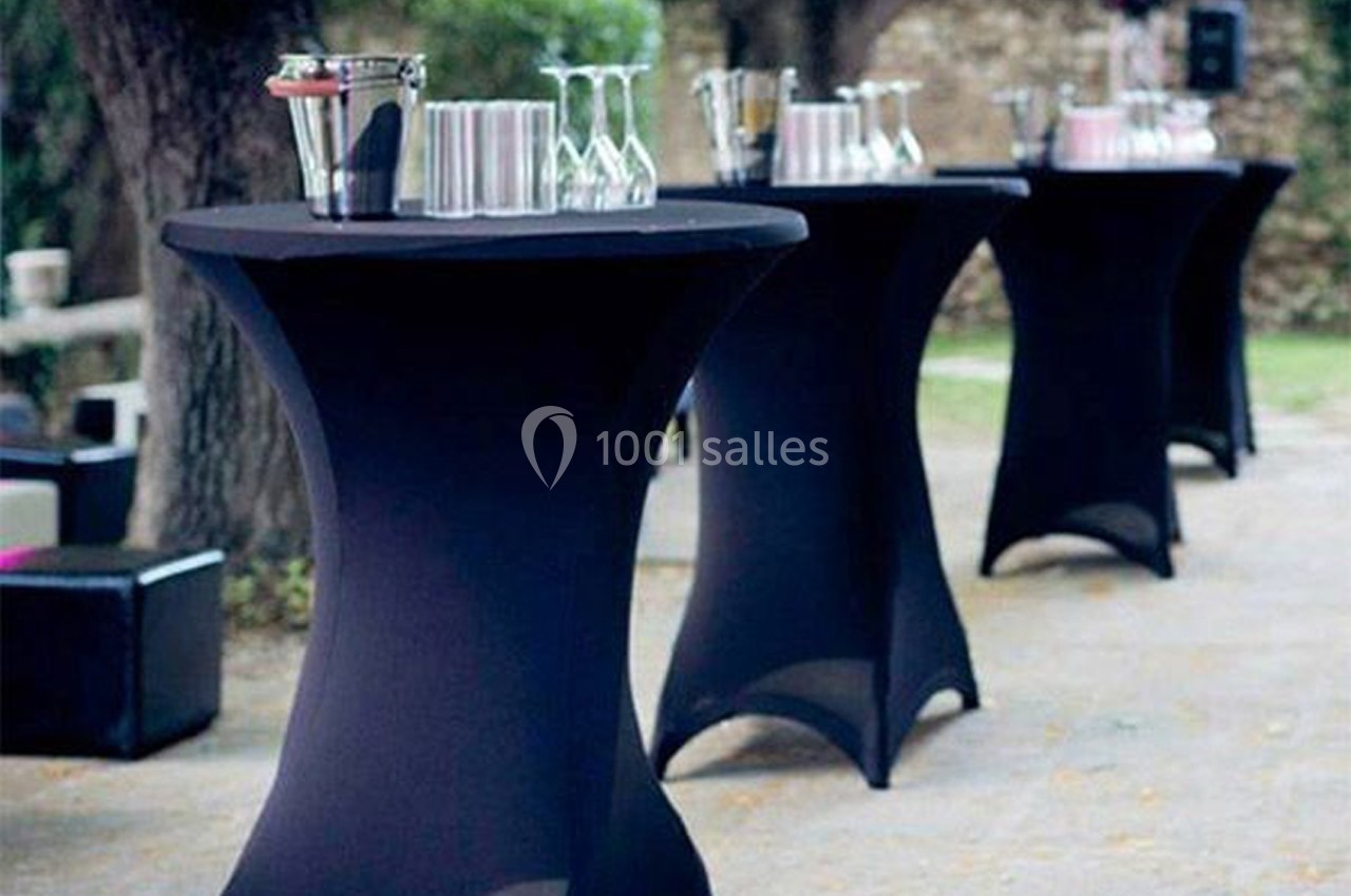 Tables hautes noires habillées de nappes, disposées en extérieur avec verres et accessoires de service.