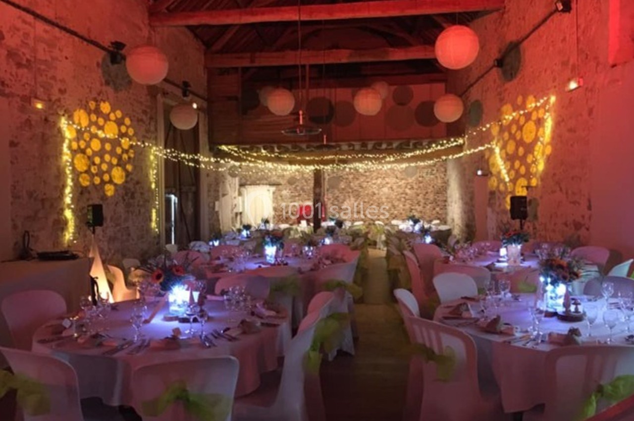 Salle de réception décorée avec des guirlandes lumineuses, des lanternes suspendues et des tables dressées pour un événement.