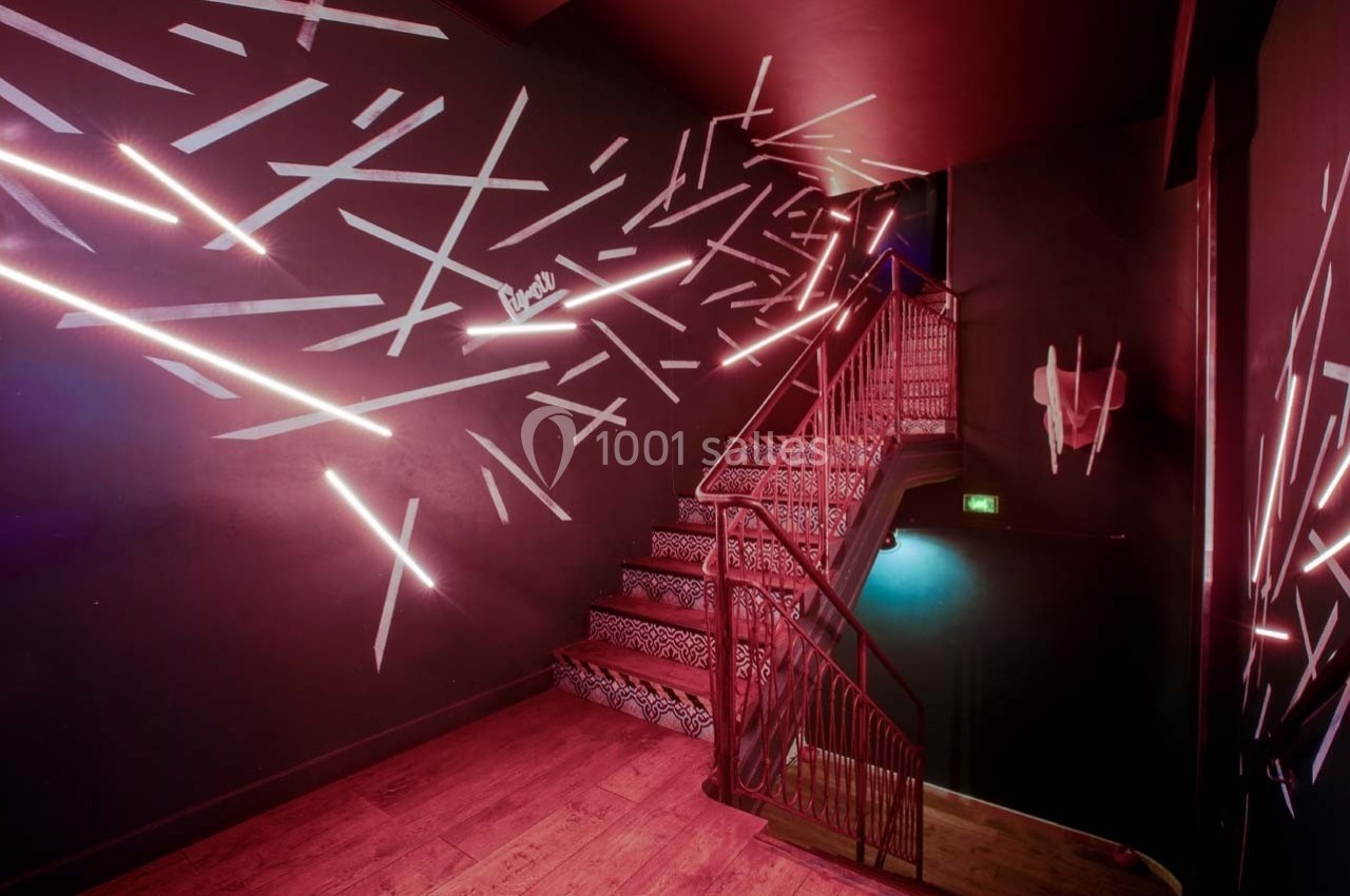 Escalier intérieur avec murs sombres décorés de néons roses et motifs géométriques, éclairage tamisé.