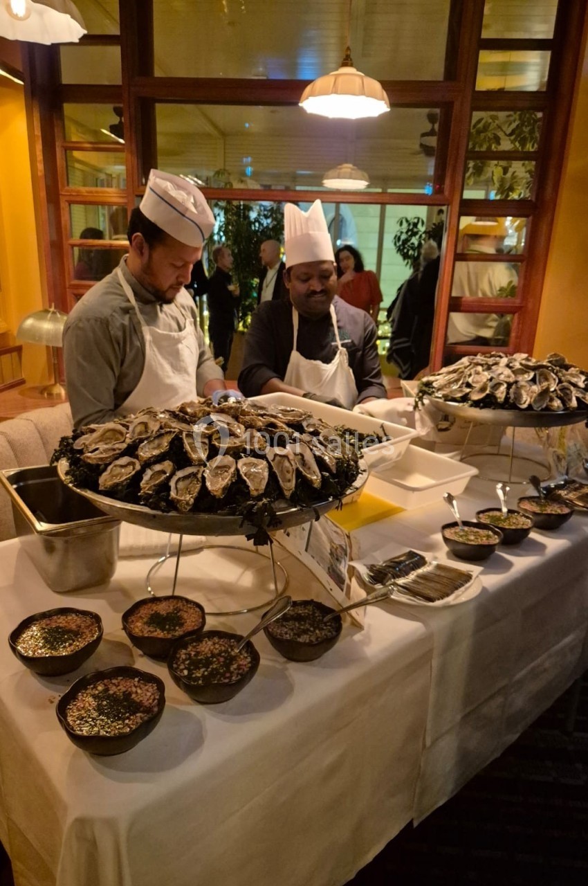 Deux chefs préparent et présentent un buffet d'huîtres fraîches sur une table garnie de condiments.
