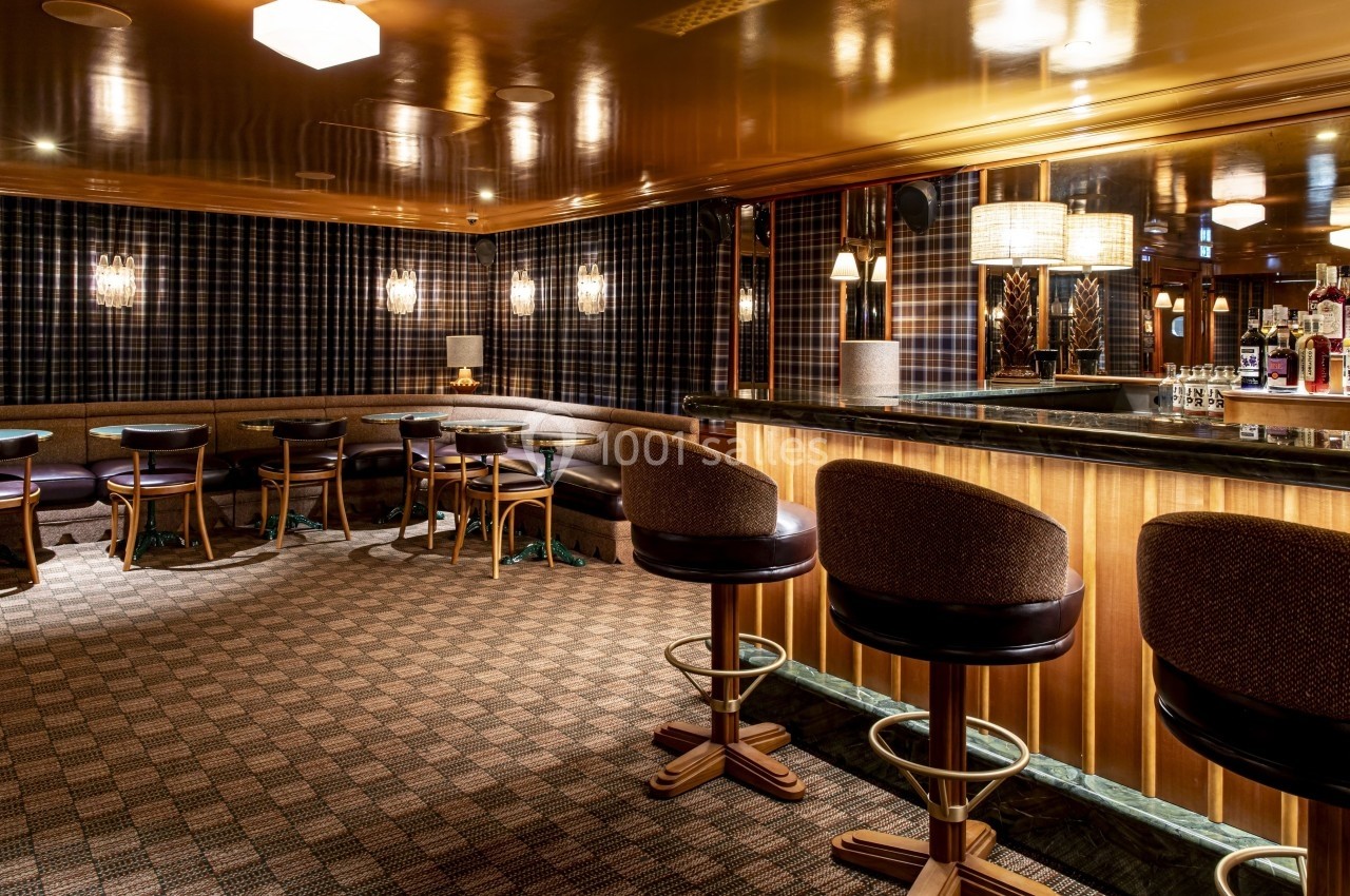 Bar intérieur élégant avec tabourets rembourrés, tables rondes, éclairage chaleureux et murs à motif écossais.