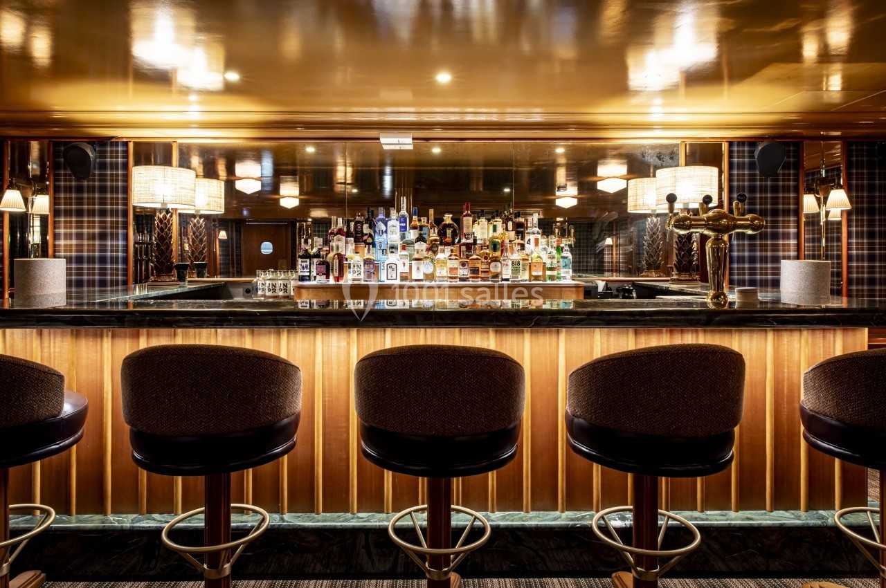 Bar élégant avec comptoir en marbre, rangée de tabourets et étagères garnies de bouteilles d'alcool en arrière-plan.