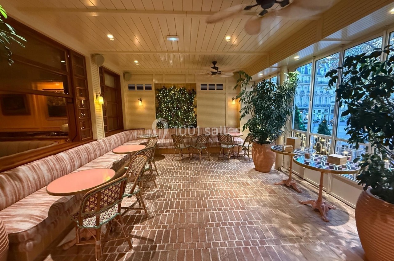 Salle lumineuse avec tables en rotin, banquettes, plantes en pot et mur décoré de végétation.