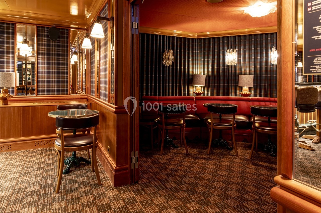 Salle avec tables et chaises en bois, banquettes rouges, murs à motif écossais et éclairage tamisé.