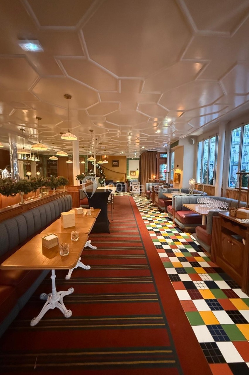 Intérieur d'un restaurant avec banquettes, tables en bois, sol coloré et grandes fenêtres donnant sur l'extérieur.