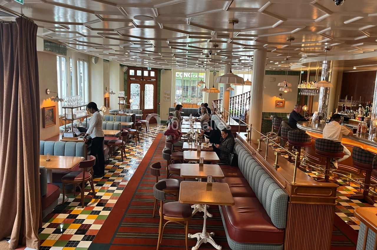 Salle de restaurant lumineuse avec des tables en bois, banquettes colorées et un sol à motifs géométriques.