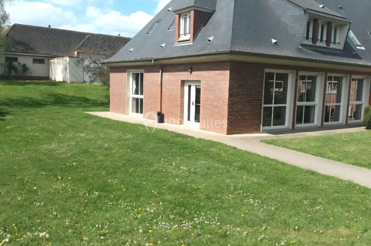 Maison en briques avec toit en ardoise, entourée d'une pelouse et d'un chemin pavé sous un ciel dégagé.