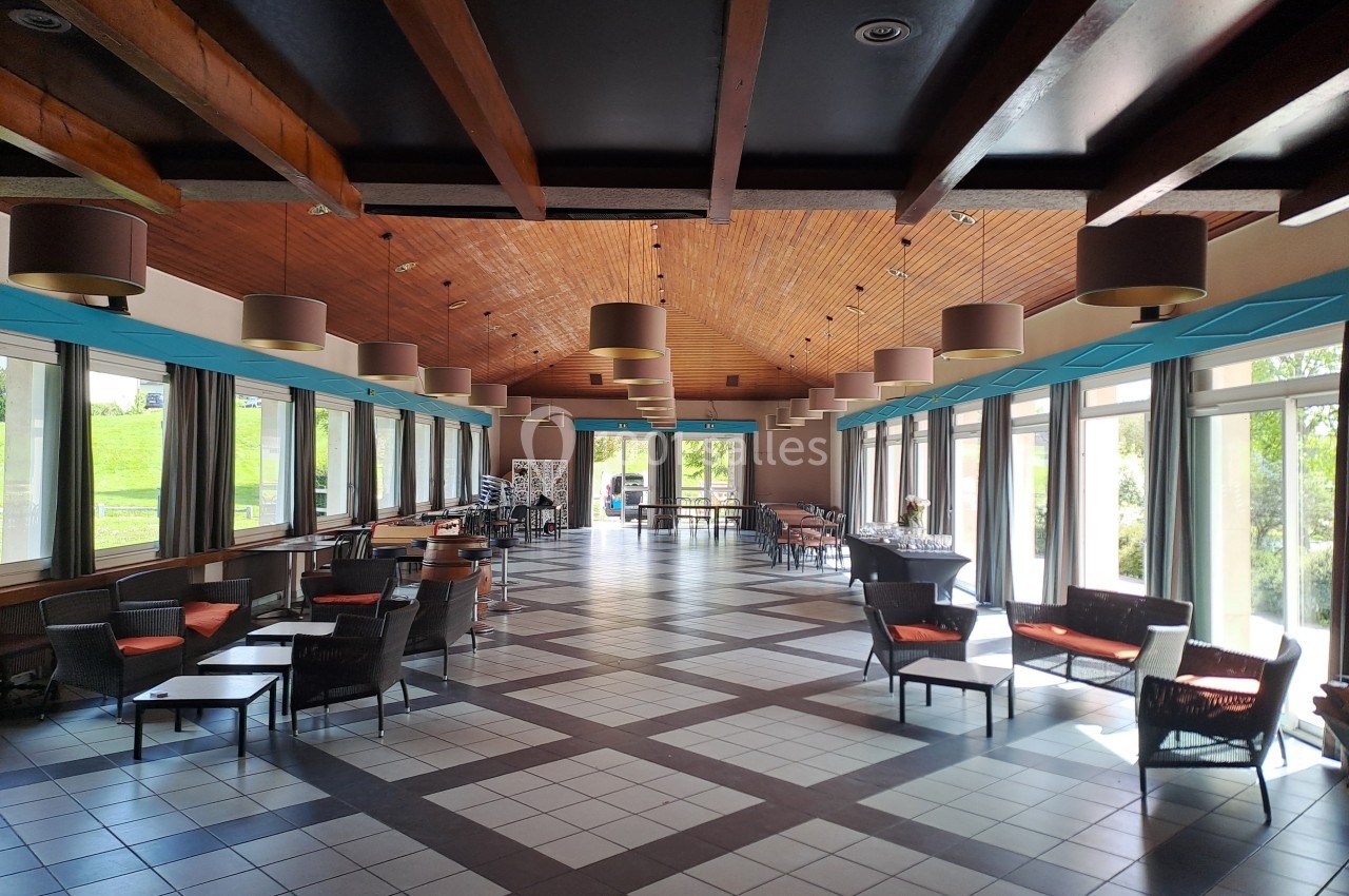 Salle spacieuse avec plafond en bois, grandes baies vitrées, mobilier moderne et lumière naturelle abondante.