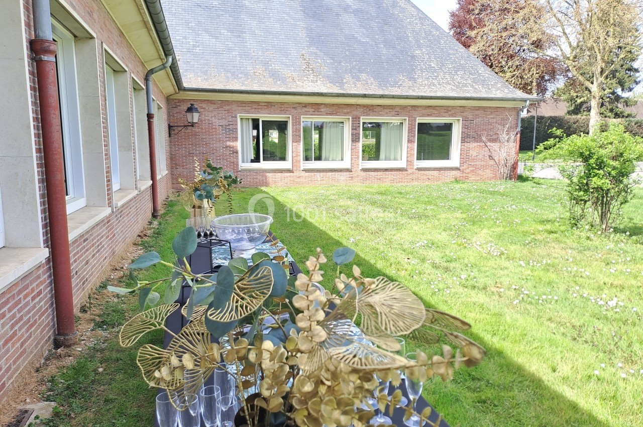Table décorée avec des plantes dorées et des verres, placée dans un jardin près d'un bâtiment en briques.