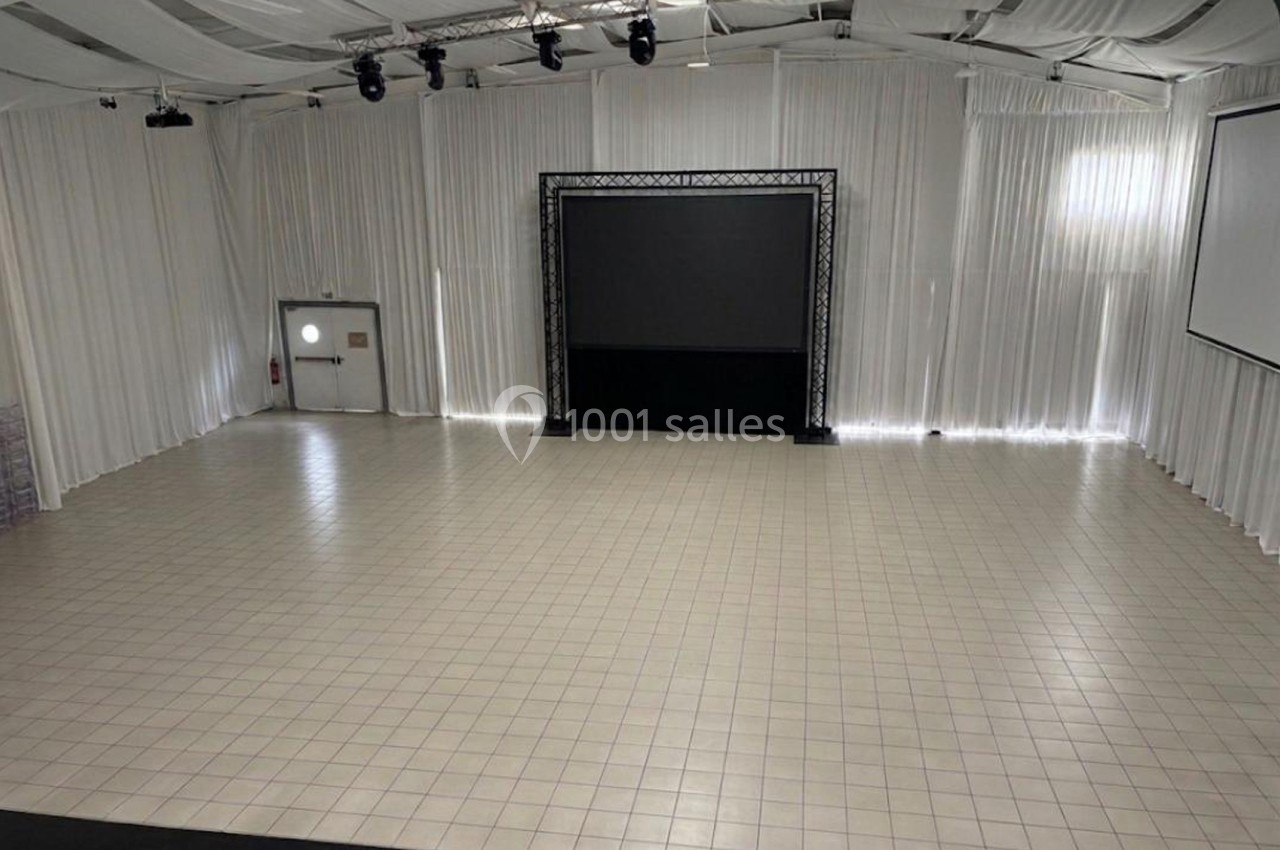 Salle vide avec sol carrelé, murs et plafond recouverts de rideaux blancs, écran noir et éclairage suspendu.