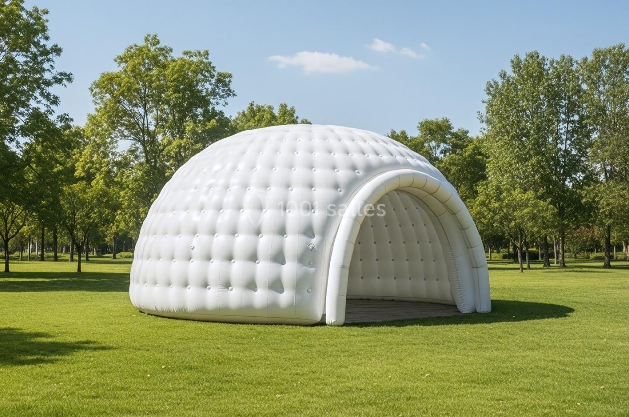 Structure gonflable blanche en forme d'igloo installée sur une pelouse dans un parc verdoyant.