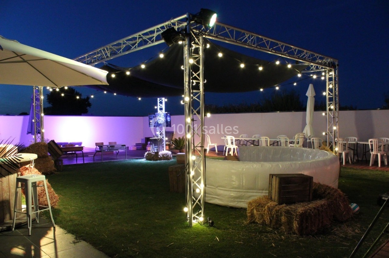 Espace extérieur décoré pour un événement nocturne avec guirlandes lumineuses, piscine gonflable et mobilier de jardin.