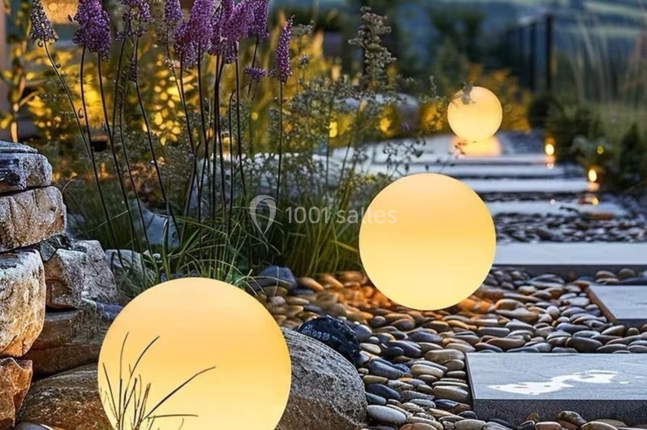 Chemin de jardin avec des galets, éclairé par des lampes sphériques lumineuses entourées de végétation.