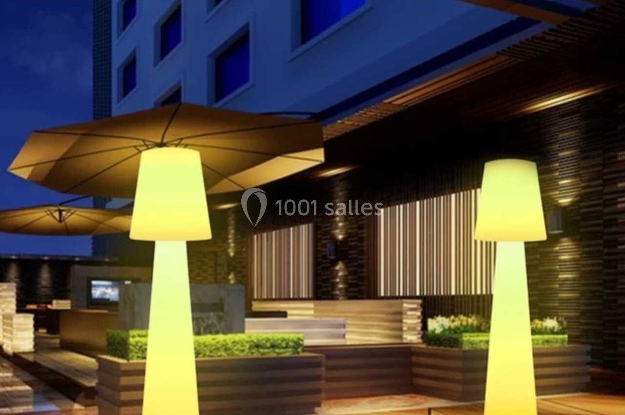 Terrasse moderne éclairée de nuit avec des lampes jaunes en forme de colonnes et des parasols.