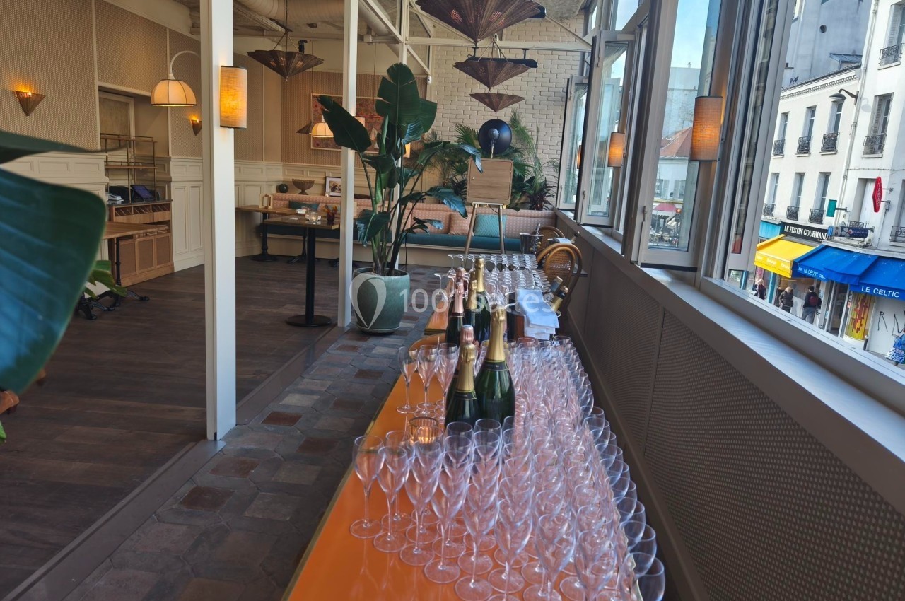 Table dressée avec des flûtes à champagne et des bouteilles, dans une salle lumineuse avec vue sur la rue.
