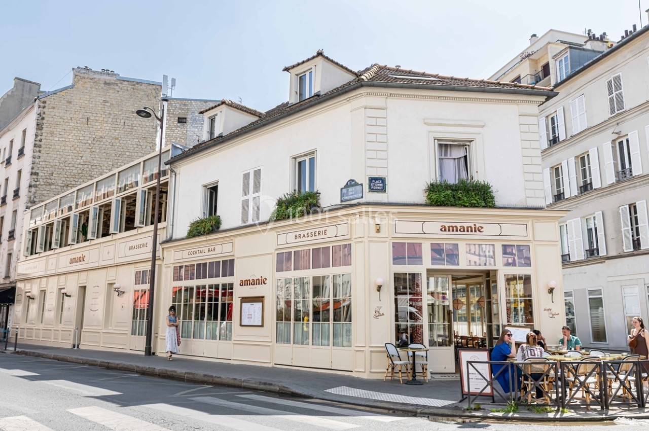 Façade d'une brasserie d'angle avec terrasse, grandes fenêtres et quelques clients assis à l'extérieur.