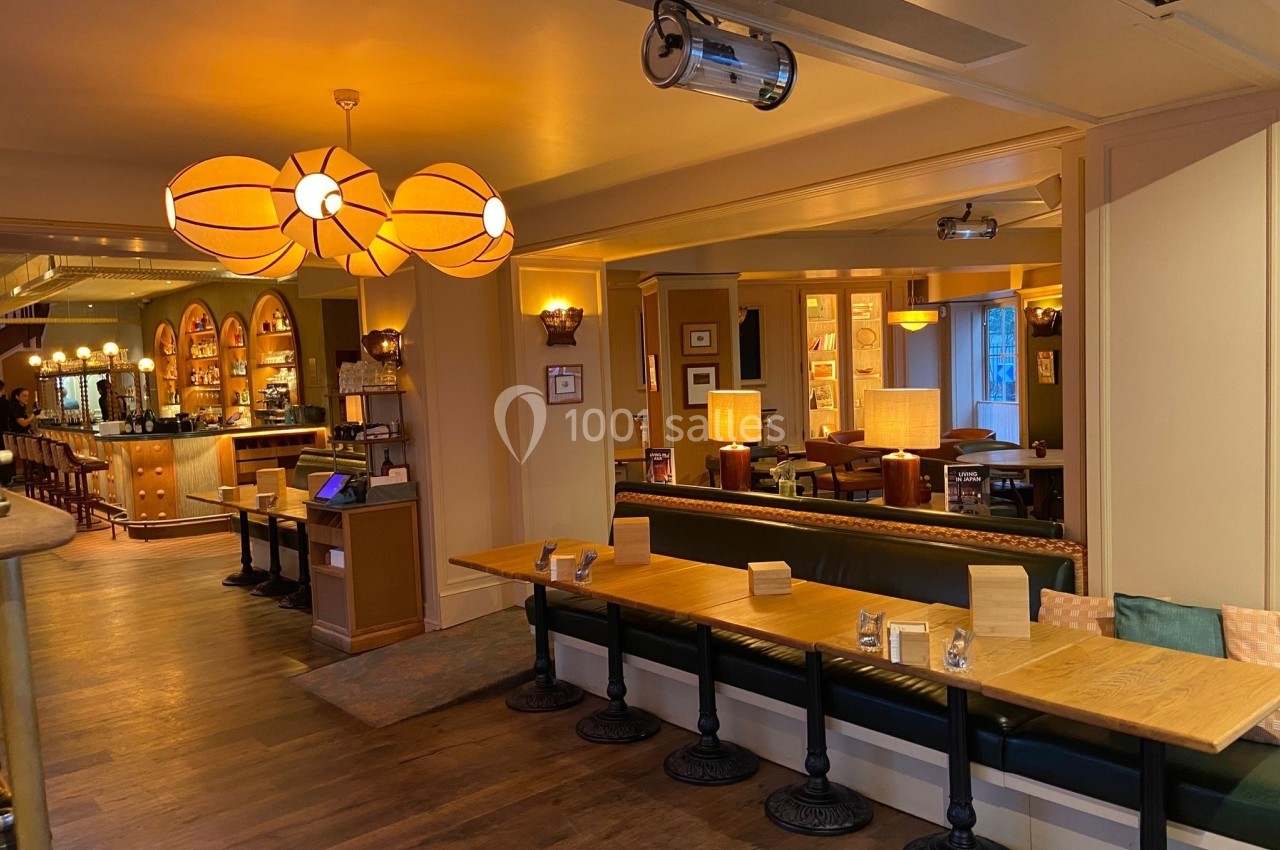 Salle de restaurant chaleureuse avec tables en bois, banquettes vertes et éclairage tamisé.