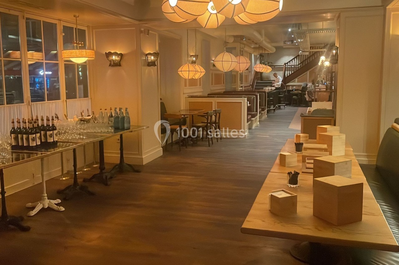 Salle de restaurant élégante avec tables en bois, éclairage chaleureux et table de service avec bouteilles et verres.