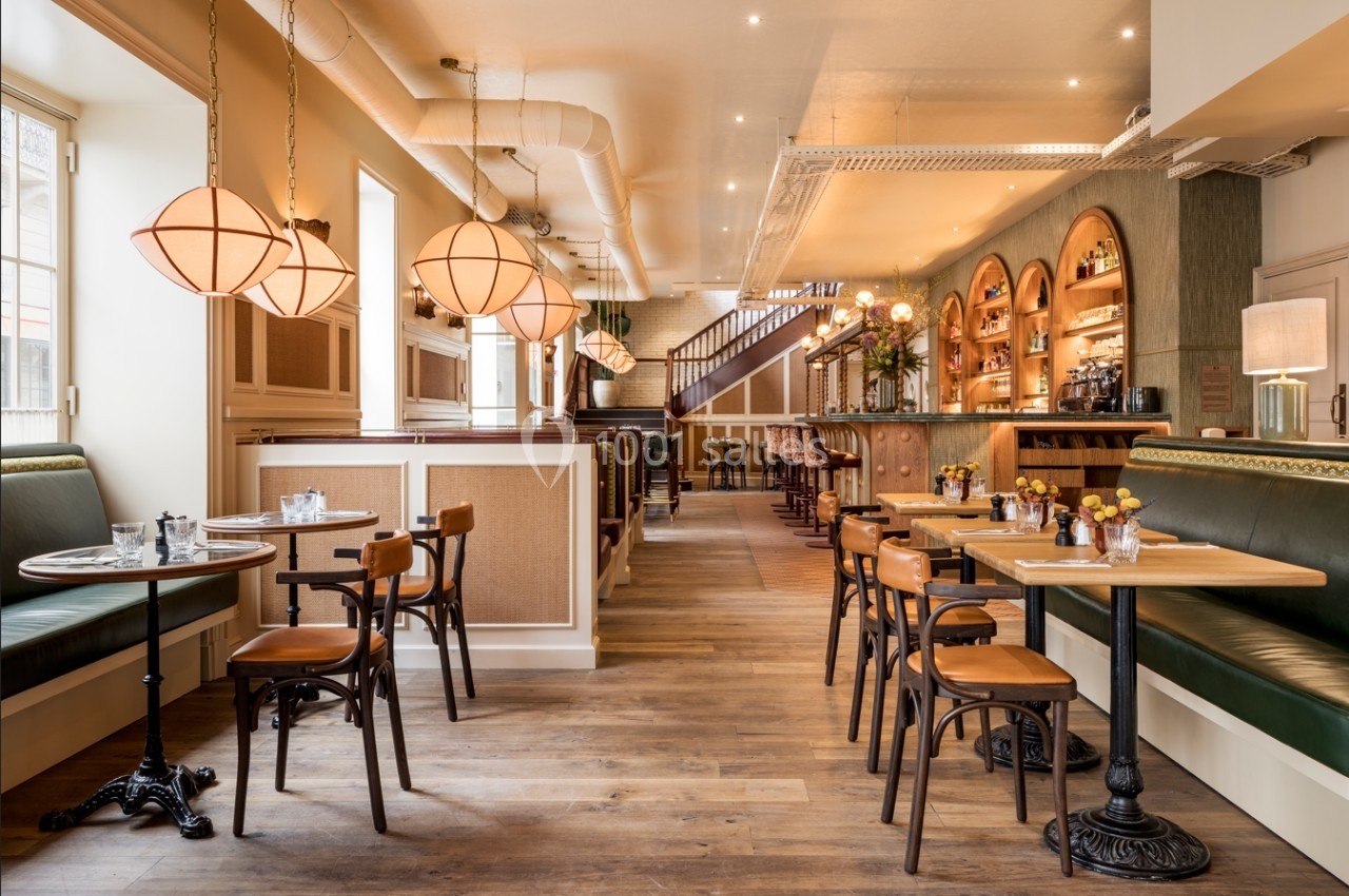 Salle de restaurant lumineuse avec tables en bois, banquettes vertes et suspensions arrondies dans un décor chaleureux.