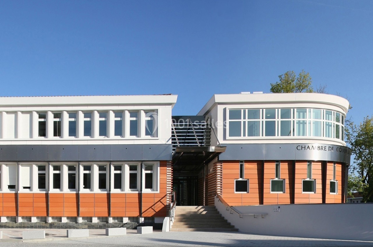 Bâtiment moderne avec façade en briques orange, grandes fenêtres et entrée principale entourée d'arbres.
