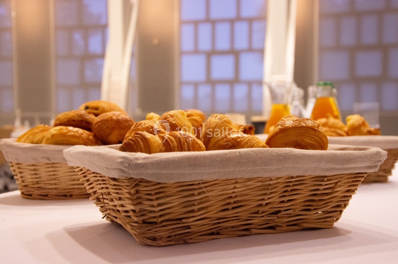 Paniers en osier remplis de viennoiseries sur une table, avec des carafes de jus d'orange en arrière-plan.