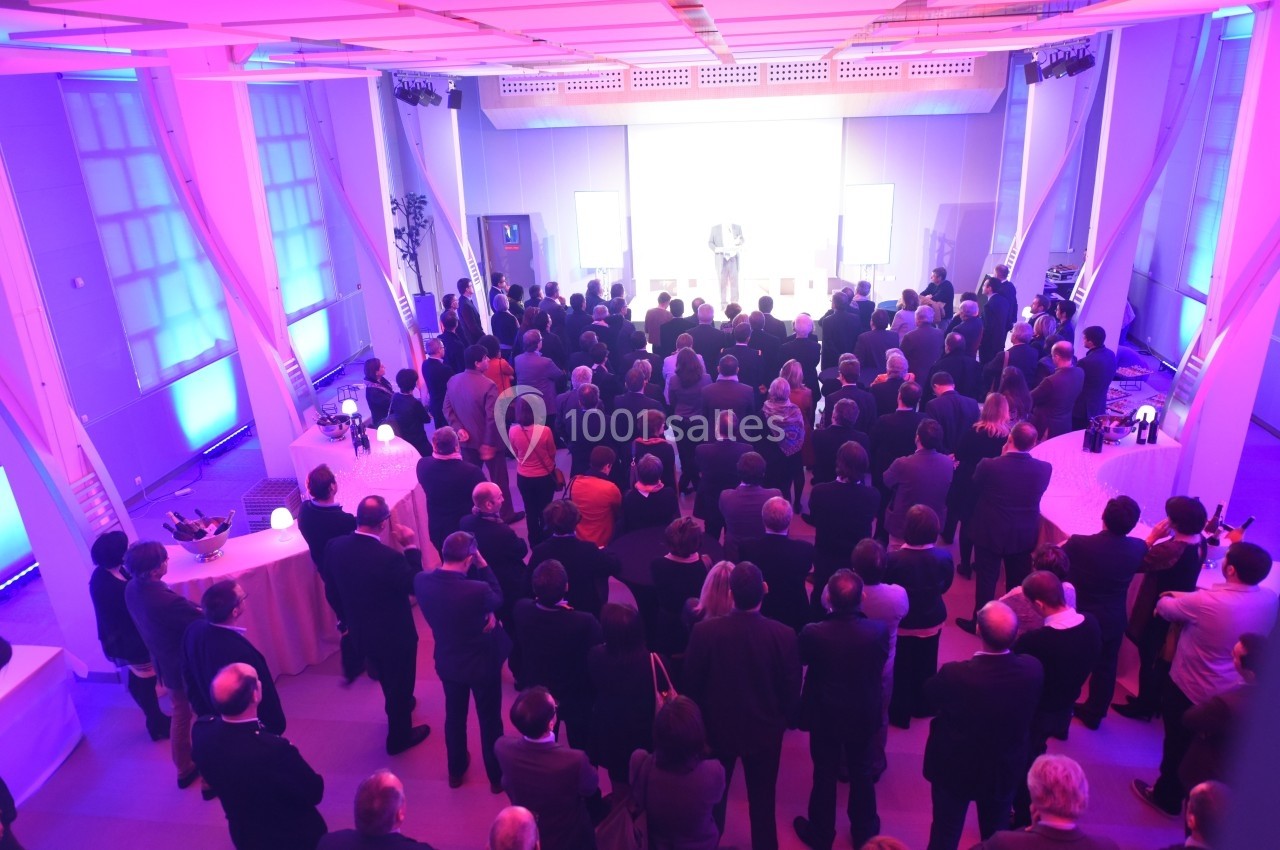 Un groupe de personnes assiste à un événement dans une salle éclairée par des lumières roses et bleues.