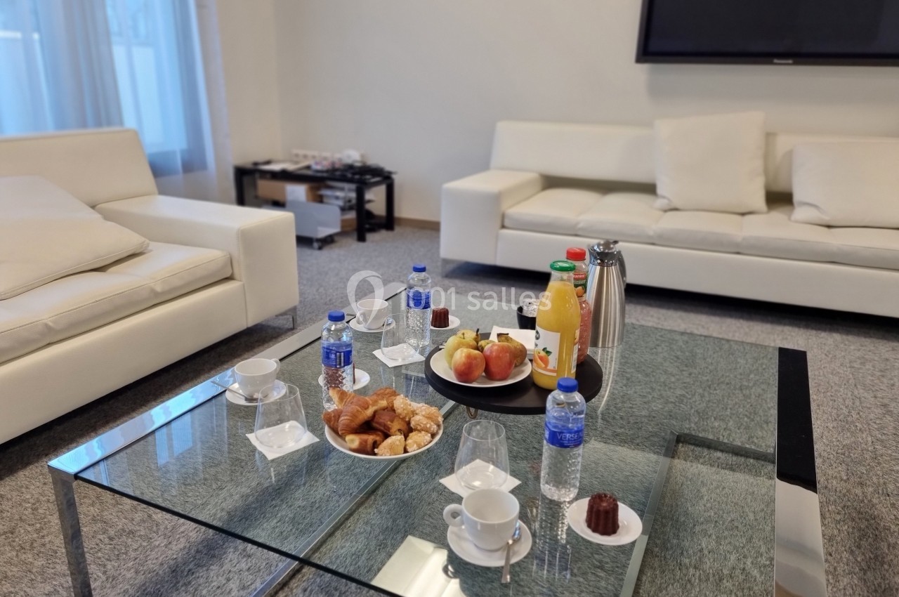 Petit-déjeuner servi sur une table basse en verre avec viennoiseries, fruits, jus, café et bouteilles d'eau.