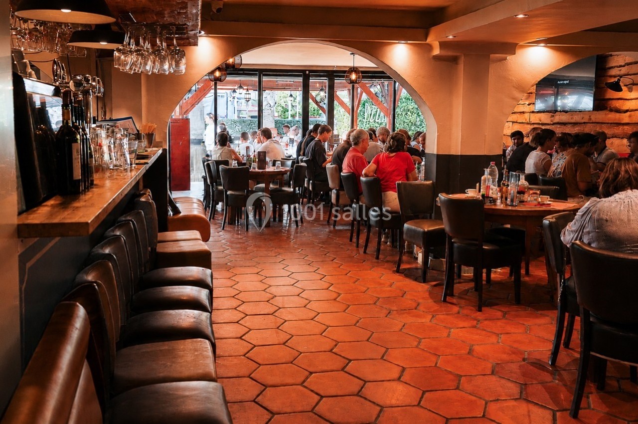 Salle de restaurant animée avec des clients assis à des tables, éclairage chaleureux et sol en carreaux orange.