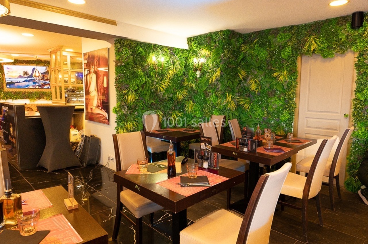Salle de restaurant lumineuse avec tables dressées, chaises blanches et mur végétal décoratif en arrière-plan.