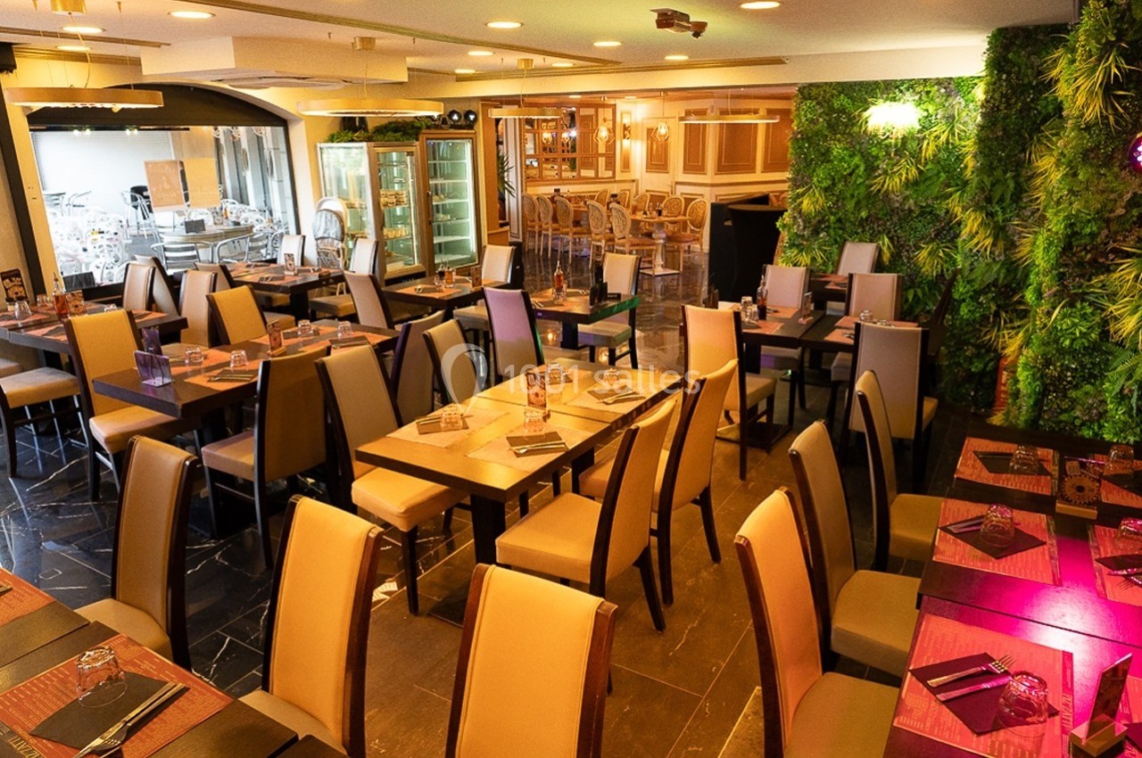 Salle de restaurant moderne avec tables dressées, chaises en cuir beige et mur végétalisé en arrière-plan.