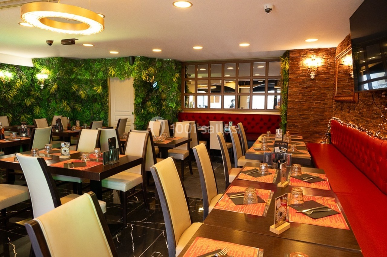 Salle de restaurant moderne avec tables dressées, chaises beige, murs végétalisés et éclairage chaleureux.