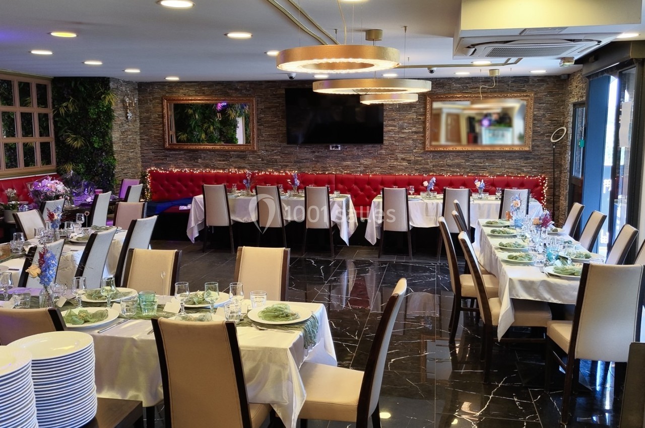 Salle de réception élégante avec tables dressées, chaises beige, banquette rouge et décoration végétale.
