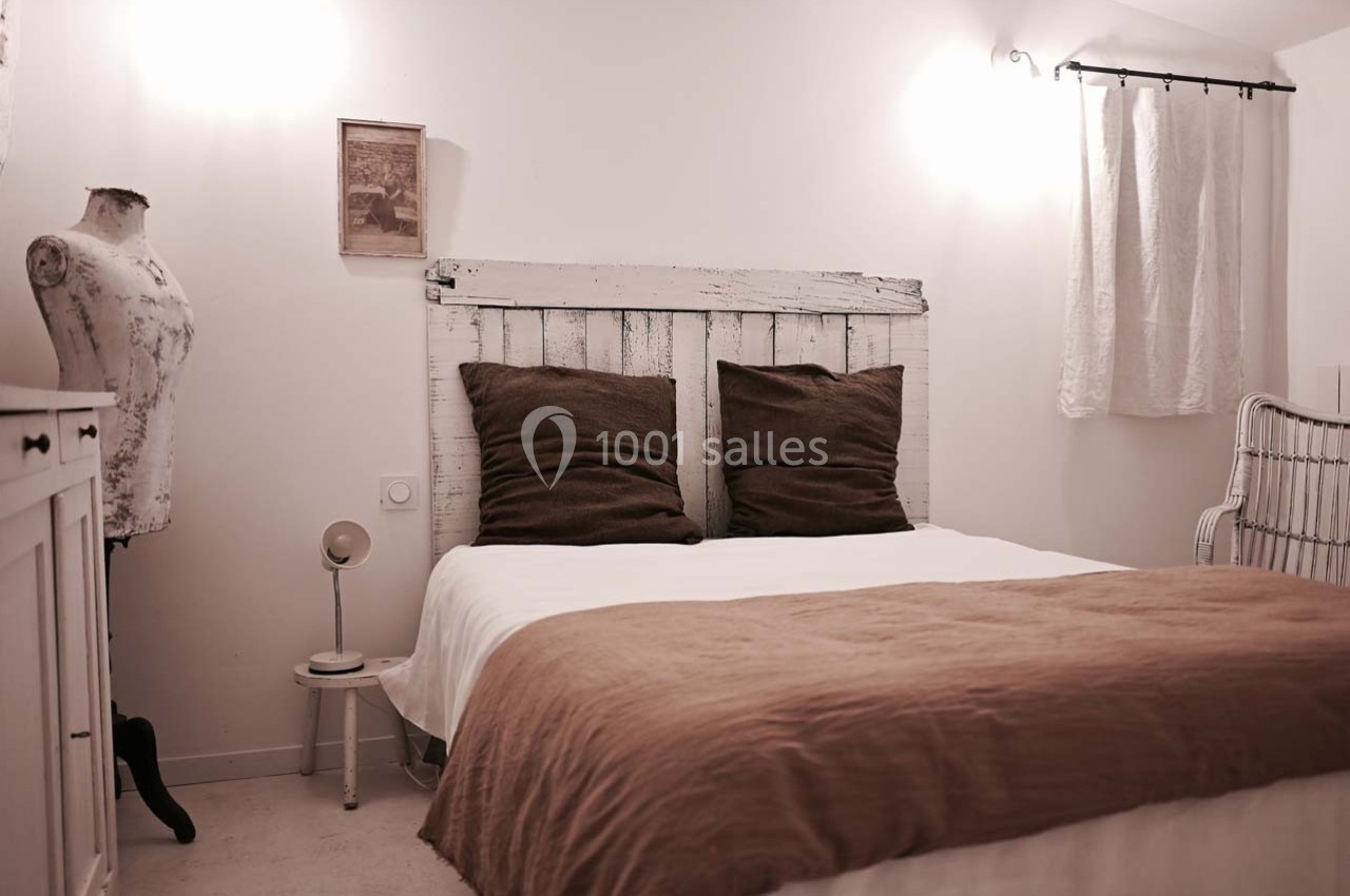 Chambre lumineuse avec lit double, tête de lit en bois blanc, coussins marron et décoration sobre.
