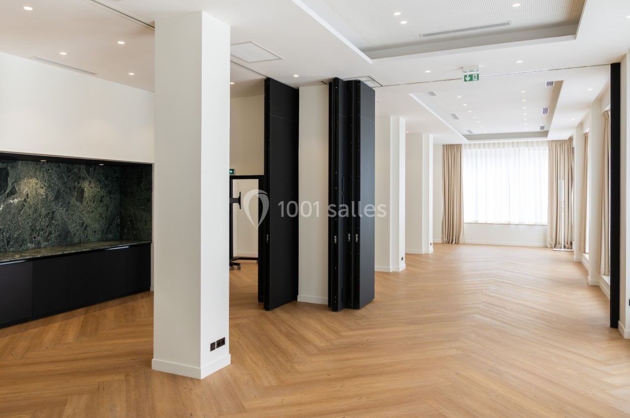 Salle lumineuse avec parquet en bois clair, cloison mobile noire, murs blancs et cuisine avec crédence en marbre vert.