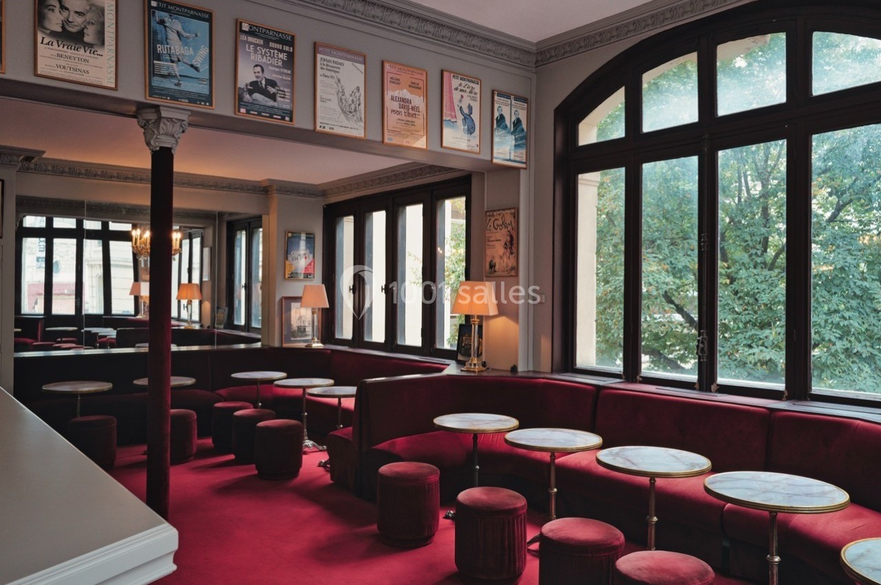 Salle de café avec banquettes rouges, petites tables rondes et affiches encadrées sur les murs, près de grandes fenêtres.