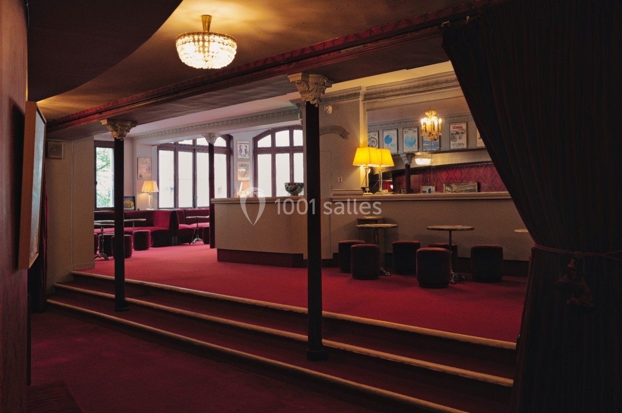 Intérieur d'un salon élégant avec moquette rouge, colonnes, bar, tables basses et éclairage chaleureux.