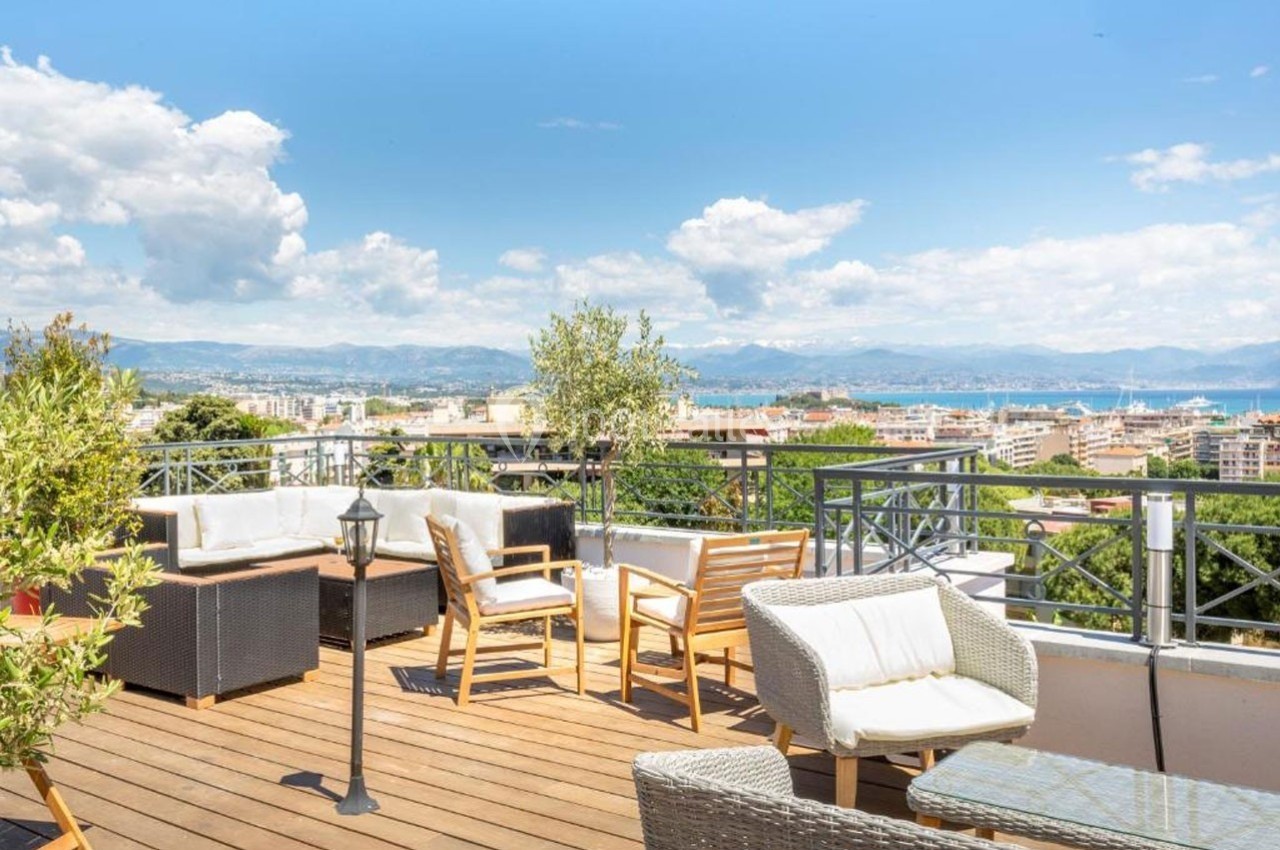 Terrasse en bois aménagée avec mobilier de jardin, vue sur une ville, des collines et la mer à l'horizon.
