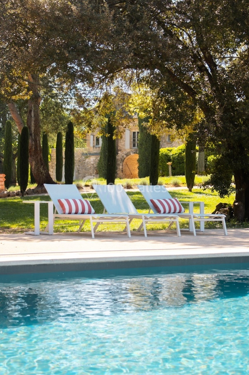 Transats alignés près d'une piscine, entourés d'arbres et de verdure, avec une maison en arrière-plan.