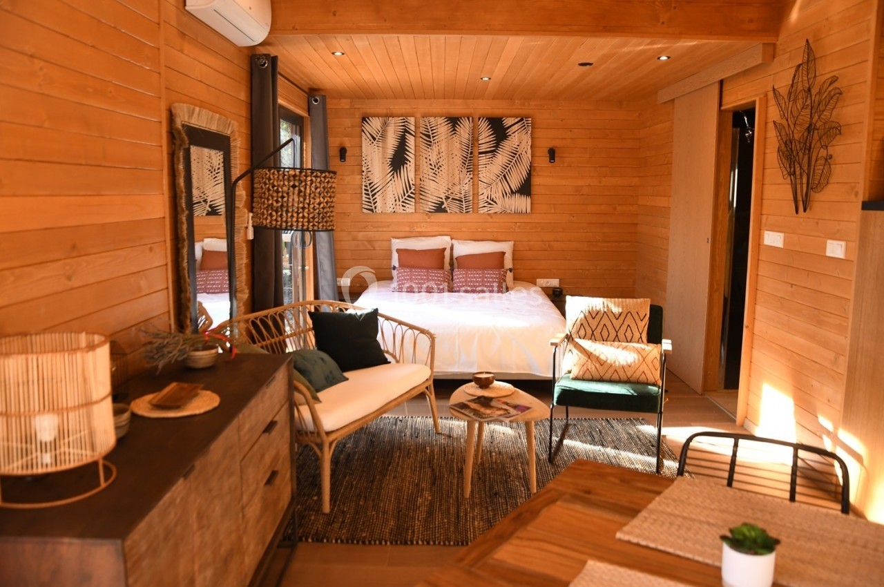 Intérieur chaleureux d'une chambre en bois avec lit double, mobilier en rotin et décoration naturelle.