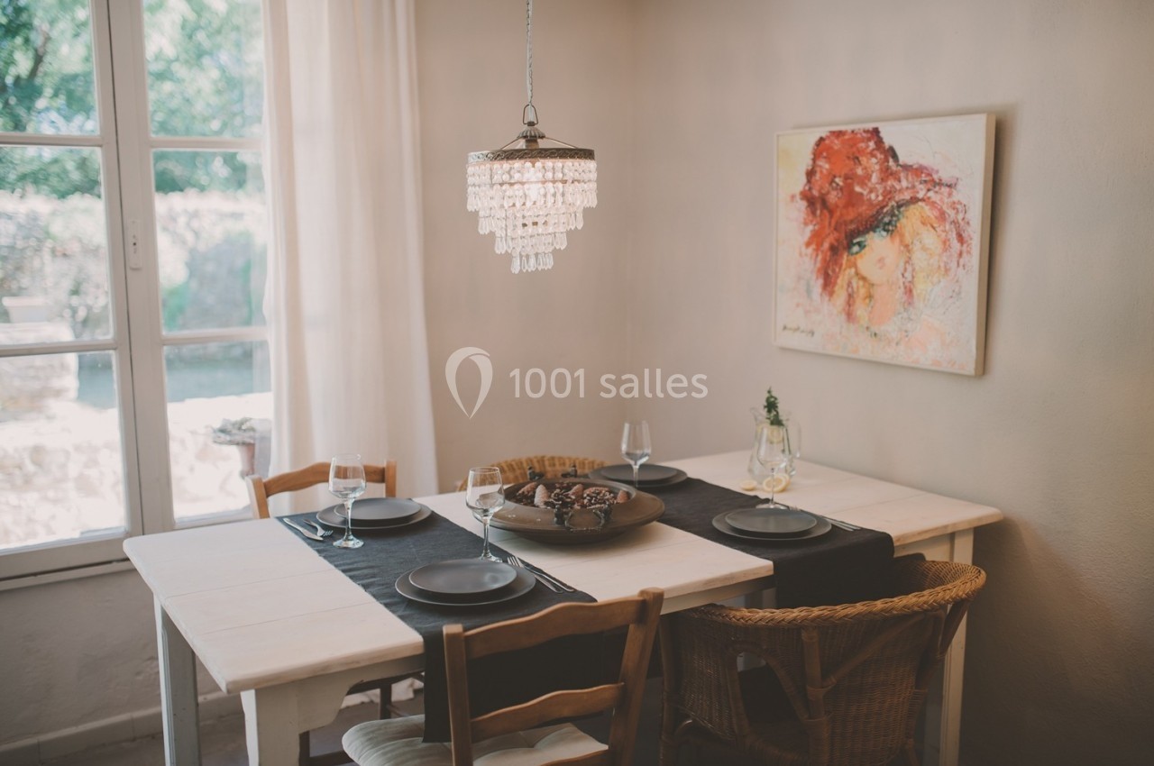 Table à manger dressée avec des assiettes noires, un chemin de table sombre et une suspension lumineuse, près d'une fenêtre.