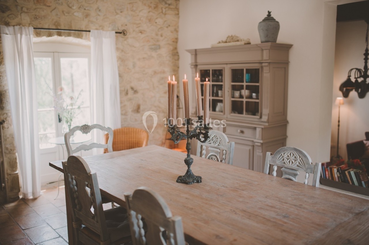 Salle à manger rustique avec table en bois, chandelier allumé, chaises sculptées et buffet en arrière-plan.