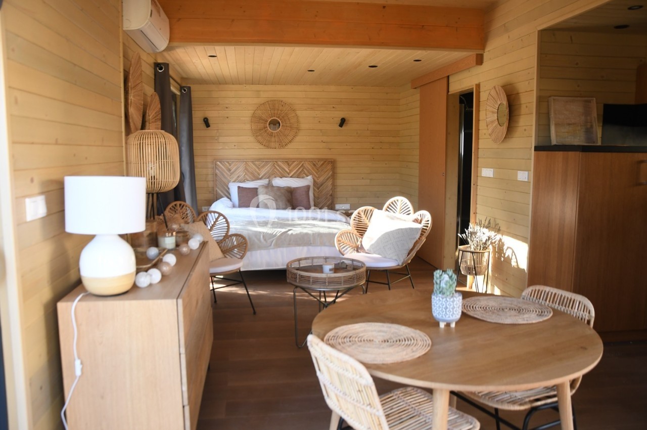 Intérieur d'un chalet en bois avec un lit double, des fauteuils en rotin, une table ronde et une décoration chaleureuse.